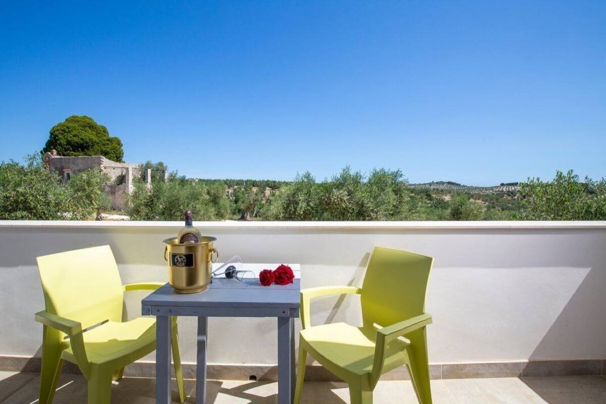 A balcony with two yellow chairs and a table, a bottle, and a red rose.