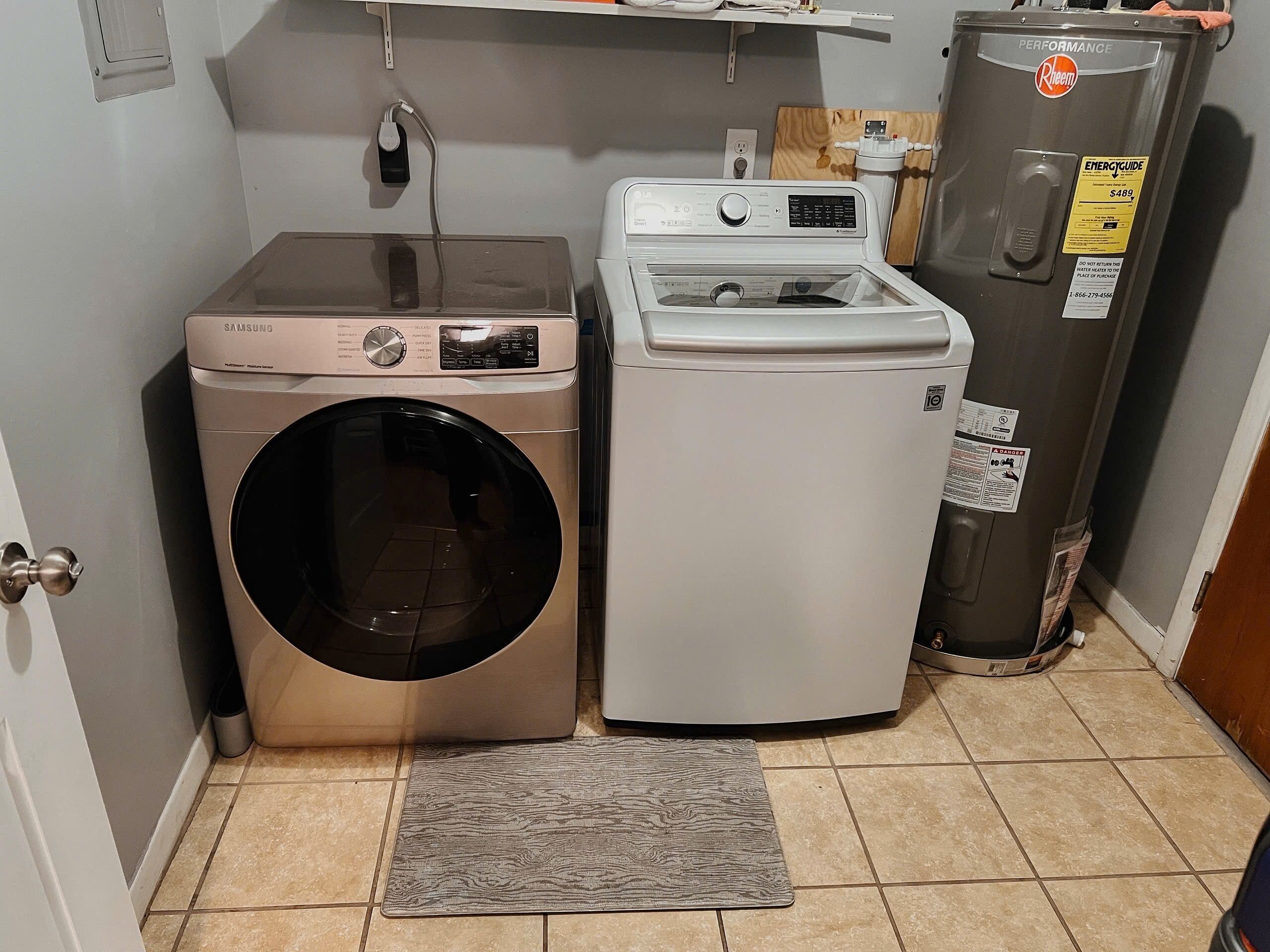 A laundry area with a Samsung washer and a Rheem dryer, a tiled floor, and a gray rug.