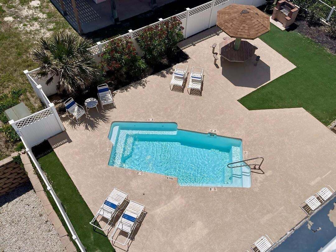 An aerial view of a swimming pool with lounge chairs, a sun umbrella, and a small garden area.