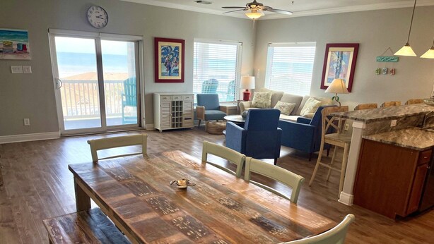 A spacious living area with a wooden dining table, blue chairs, a sofa, and a kitchen area with a marble countertop. - Beachgate Condo Suites And Hotel 341+342 4 Bedroom Condo (Port Aransas)