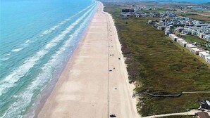 An aerial view of a beach with a long stretch of sand, a few buildings, and a road running parallel to the beach. - Beachgate Condo Suites And Hotel 341+342 4 Bedroom Condo (Port Aransas)