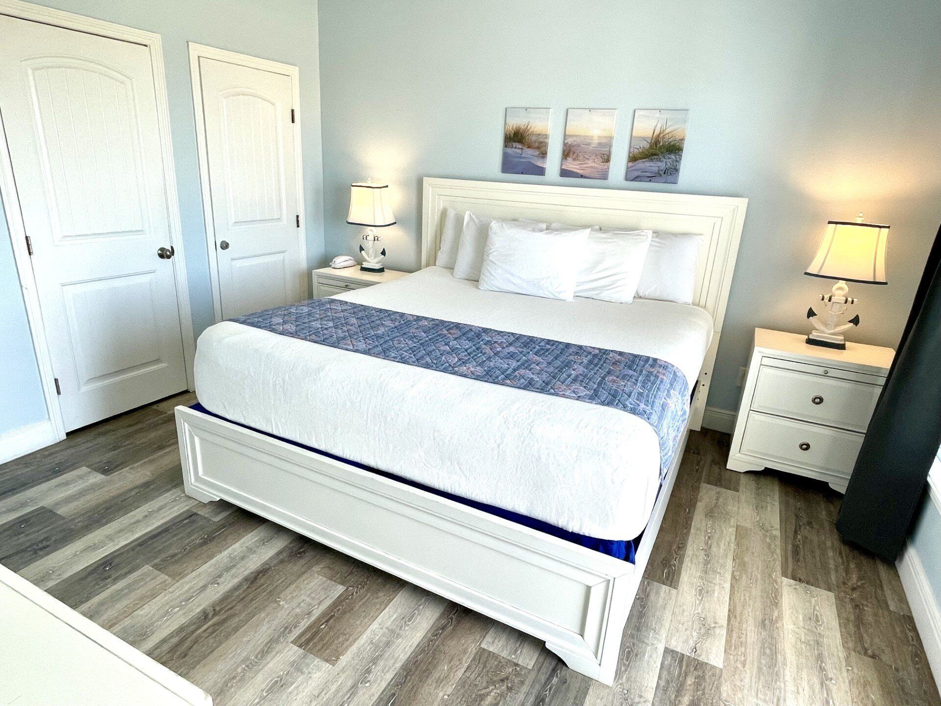 A hotel room with a large bed, two bedside tables, a nightstand, and a wall-mounted lamp.