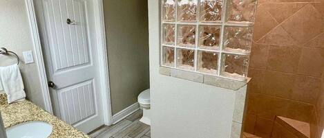 A bathroom with a white door, a sink with a granite countertop, a glass shower enclosure, and a toilet.