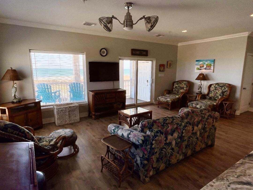 A living room with a sofa, chairs, a TV, and a view of the ocean through large windows.
