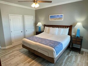 A neatly arranged bedroom with a large bed, two bedside tables with lamps, a ceiling fan, and a framed picture on the wall. - Beachgate Condo Suites And Hotel 341 2 Bedroom Condo (Port Aransas)