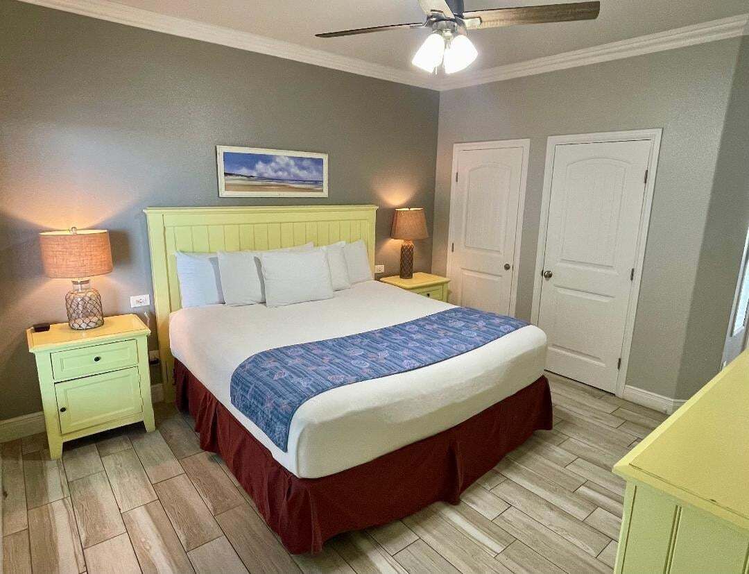 A bedroom with a bed, two nightstands, a ceiling fan, and two doors.