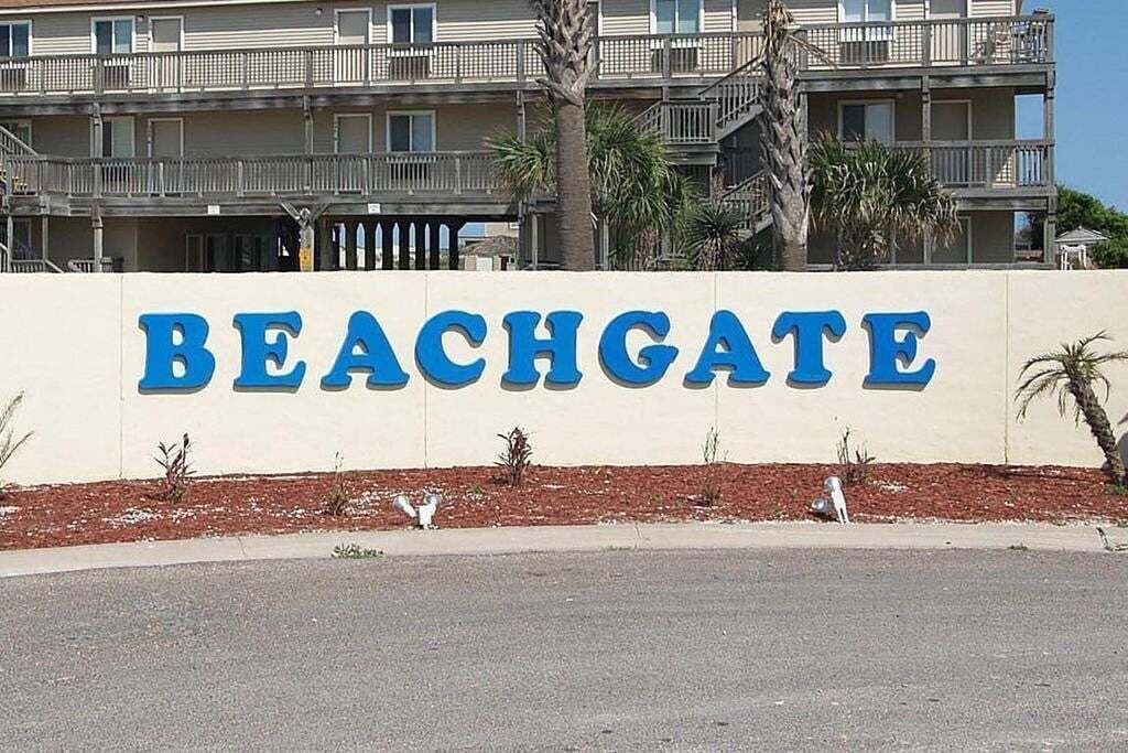 Et skilt med ordet "BEACHGATE" i store blå bogstaver på en beige v æg.