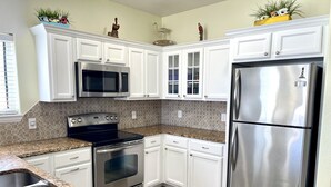A kitchen with white cabinets, stainless steel appliances, granite countertops, and a wooden floor. - Beachgate Condo Suites And Hotel 322 2 Bedroom Condo (Port Aransas)