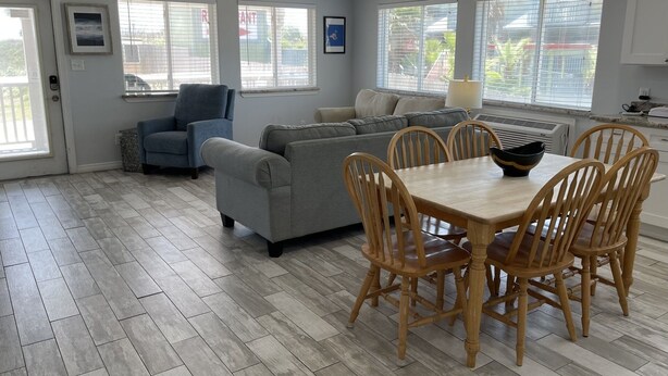 A spacious living area with a grey sofa, blue armchair, and a dining table with wooden chairs. - Beachgate Condo Suites And Hotel 217+219 2 Bedroom Condo (Port Aransas)