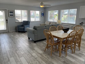 A spacious living area with a grey sofa, blue armchair, and a dining table with wooden chairs. - Beachgate Condo Suites And Hotel 217+219 2 Bedroom Condo (Port Aransas)