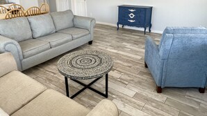 A living room with a grey sofa, a blue armchair, a round coffee table, and a TV on the wall. - Beachgate Condo Suites And Hotel 217+219 2 Bedroom Condo (Port Aransas)