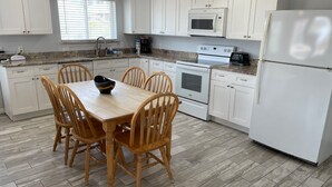 A kitchen with white cabinets, a microwave, a stove, a refrigerator, and a dining table with chairs. - Beachgate Condo Suites And Hotel 217+219 2 Bedroom Condo (Port Aransas)