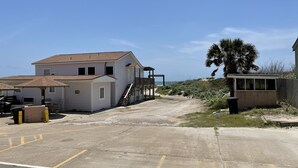 A beachfront property with a white building, a covered outdoor area, and a dirt road leading to the beach. - Beachgate Condo Suites And Hotel 217+219 2 Bedroom Condo (Port Aransas)