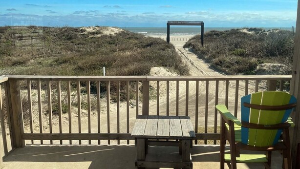 A wooden deck with a table and chairs overlooking a beach with a dune path. - Beachgate Condo Suites And Hotel 121 1 Bedroom Condo (Port Aransas)