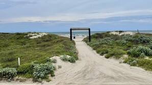 A sandy pathway leading to a beach with a wooden structure in the center. - Beachgate Condo Suites And Hotel 121 1 Bedroom Condo (Port Aransas)