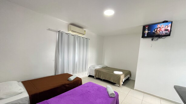 A hotel room with two beds, a TV mounted on the wall, a window with curtains, and a ceiling fan. - Pousada Anadia (Anadia)