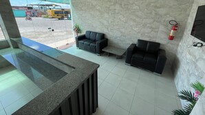 A reception area with a marble wall, two black sofas, a small table, a fire extinguisher, and a TV mounted on the wall. - Pousada Anadia (Anadia)