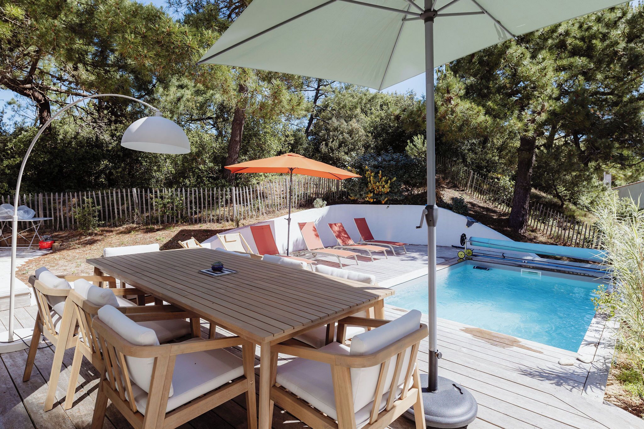 A wooden deck with a pool, lounge chairs, and an umbrella.
