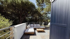 Un espace extérieur aménagé avec un canapé et une table en bois, entouré d’arbres et d’une rambarde en métal.