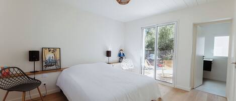A bedroom with a large bed, a chair, a picture frame, a lamp, and a view through a glass door.