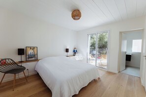 A bedroom with a large bed, a chair, a picture frame, a lamp, and a view through a glass door. - Villa La Canopée - Ile d'Oléron - Chaucre - 8 pers - swimming pool (Saint-Georges-d'Oléron)