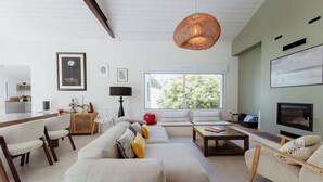 Un salon moderne comprenant un canapé, des fauteuils, une table basse, un téléviseur et une grande fenêtre donnant sur un paysage arboré.