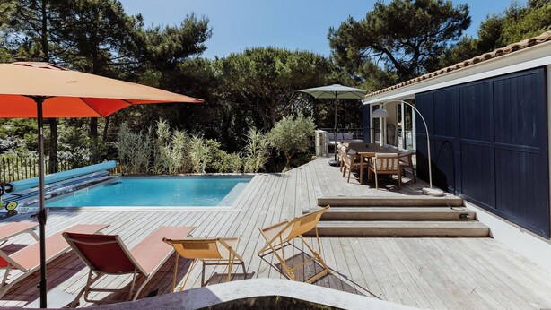 Une terrasse en bois avec une piscine, des chaises longues et des parasols.