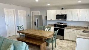 Una cocina compacta con gabinetes blancos, un refrigerador de acero inoxidable, un microondas y una estufa. Hay una mesa de comedor de madera con sillas.