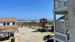 Una propiedad frente a la playa con balcón con vistas al océano, un patio cubierto con mobiliario exterior y una pequeña construcción cerca de la playa.