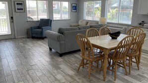 A spacious living area with a grey sofa, blue armchair, and a dining table with wooden chairs.