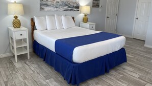 A neatly arranged bedroom with a bed, two nightstands, a painting, and a door.