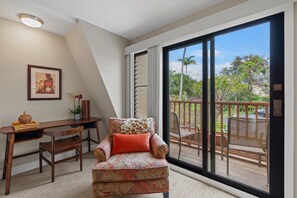 Ein Zimmer mit Schreibtisch, Stuhl und einer großen Glasschiebetür, die auf einen Balkon im Freien führt.