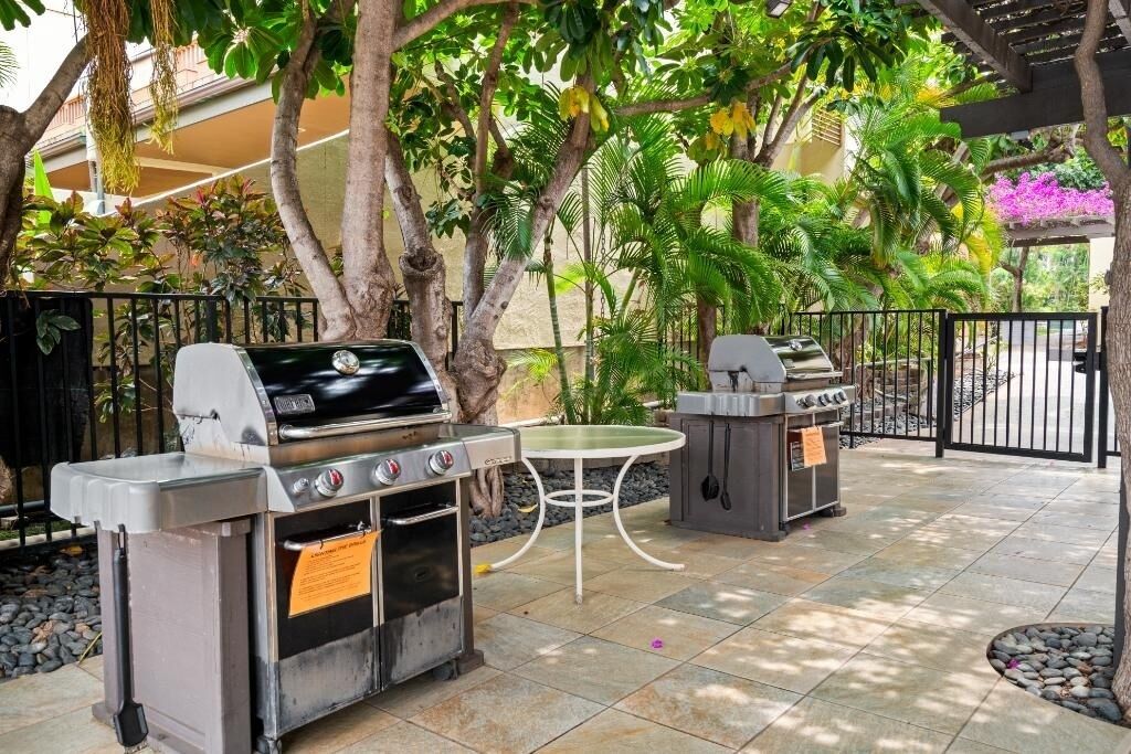 An outdoor patio with a grill station, a table, and a seating area surrounded by trees and plants.
