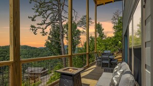 A wooden deck with a fire pit, outdoor furniture, and a scenic view of trees and mountains.