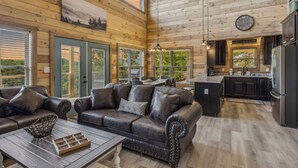 A spacious living area with a large leather sofa, a coffee table, and a view of the kitchen.