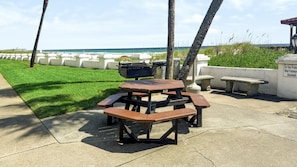 Une table de pique-nique avec des bancs, un barbecue et une vue sur l’océan.