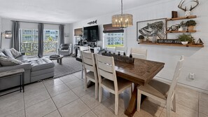 Una sala de estar moderna con comedor, ventanas amplias y una cocina al fondo.