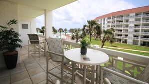Un balcon avec une table et des chaises, un pot de fleurs et une vue sur un immeuble d’hôtel et des palmiers.