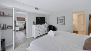 Une chambre moderne avec un grand lit, un téléviseur à écran plat, une commode blanche et une porte donnant sur une salle de bain.