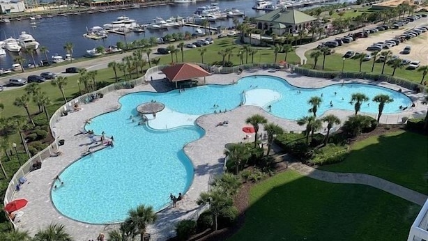 A large, irregularly shaped swimming pool with multiple sections, surrounded by palm trees and a parking lot. - River Crossing #1134 2 Bedroom Condo (North Myrtle Beach)