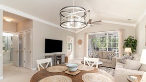 A spacious living room with a wooden dining table, sofas, and a television. - River Crossing #1134 2 Bedroom Condo (North Myrtle Beach)