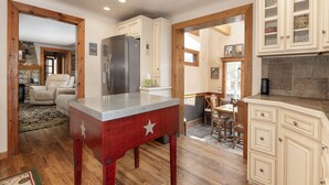 Una cocina con armarios de madera, un refrigerador, una mesa de comedor con sillas y piso de madera.