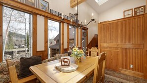 Un comedor acogedor con una mesa de madera, sillas y un banco. Un candelabro cuelga arriba, y una ventana ofrece vistas al exterior.