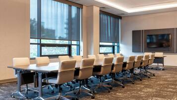A conference room with a long table, multiple chairs, large windows, and a flat-screen TV.