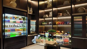 Un hall d’hôtel moderne doté d’un présentoir réfrigéré pour les boissons, de quelques étagères où sont disposés des en-cas et des produits alimentaires, et d’une petite table sur laquelle sont posées des brochures.