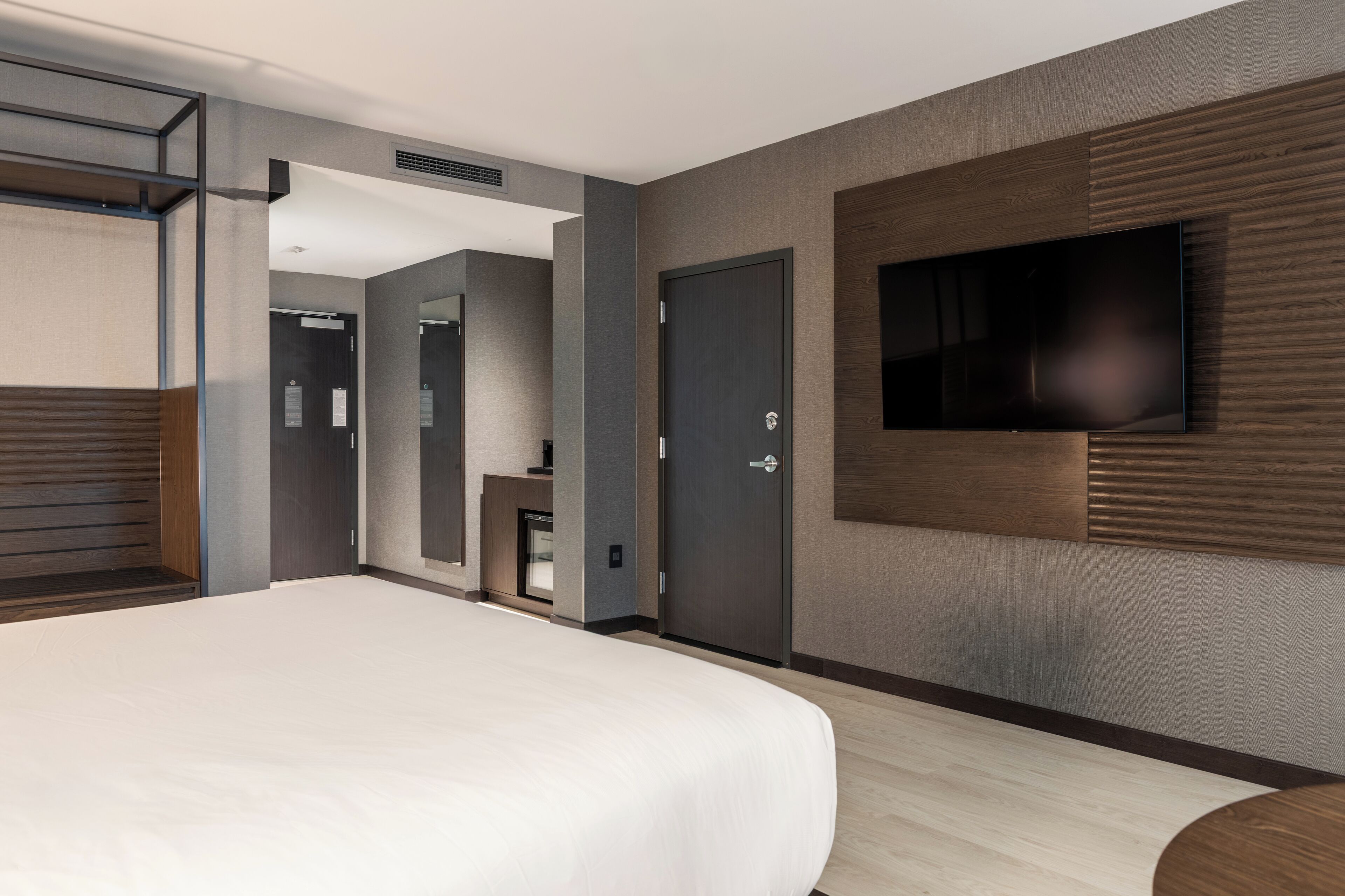 A modern hotel room with a large bed, a flat-screen TV mounted on the wall, and a wooden accent wall.