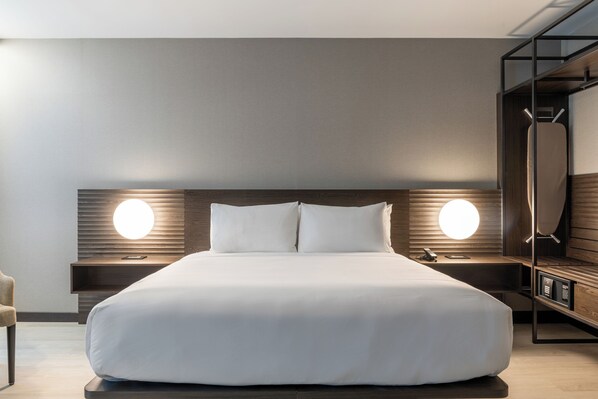 Quarto de hotel moderno com uma cama grande, duas mesas de cabeceira e um guarda-roupa embutido.