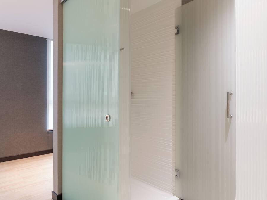 Una habitación de hotel con piso de madera, puerta de vidrio y pared blanca.