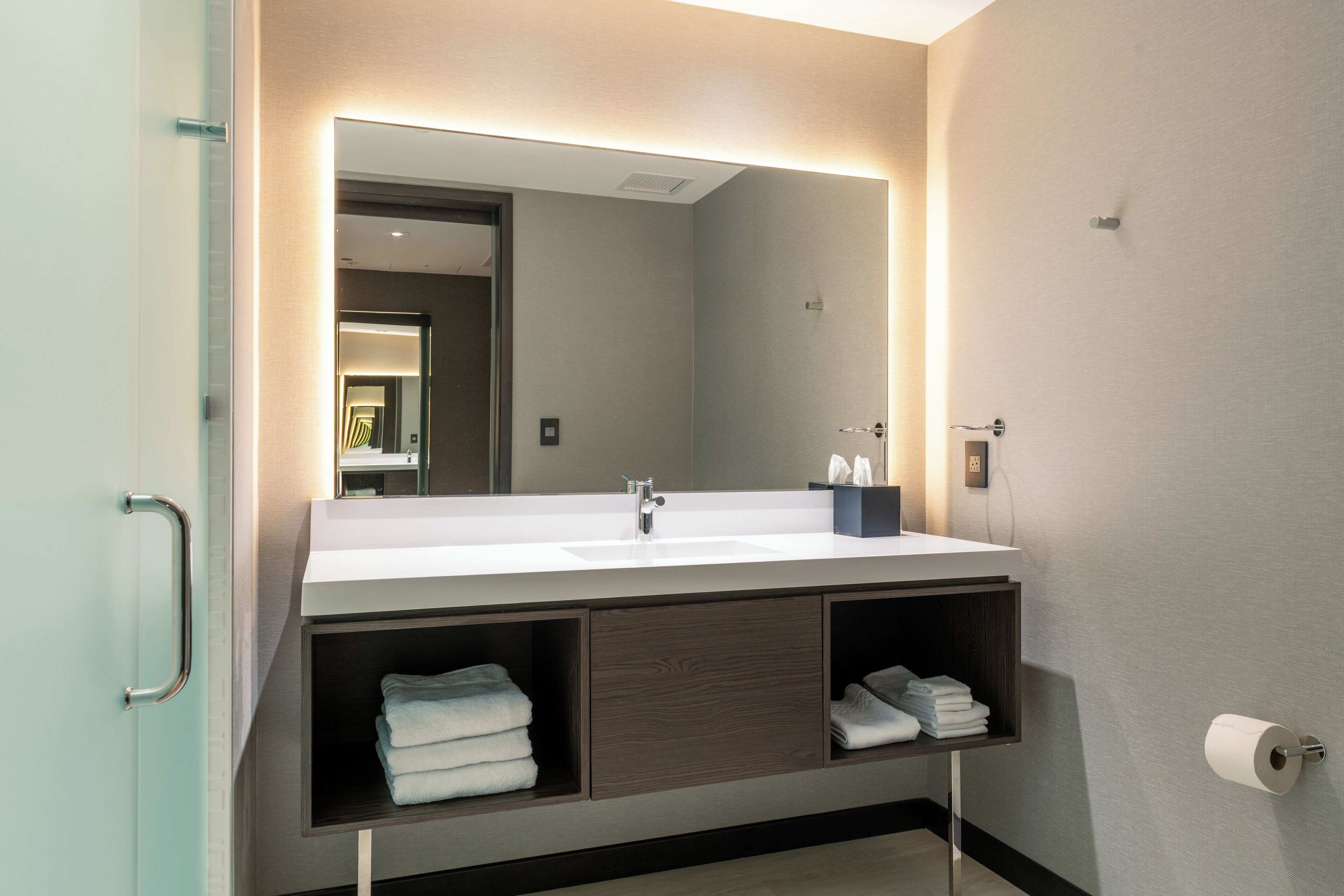 A modern bathroom with a large mirror, white sink, and built-in towel racks.