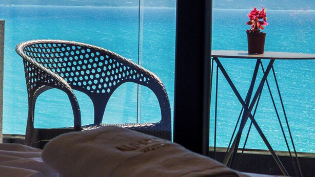 A room with a view of the sea, a chair, a small table with a potted plant, and folded towels. - Alpaso Hotel (Sarande)